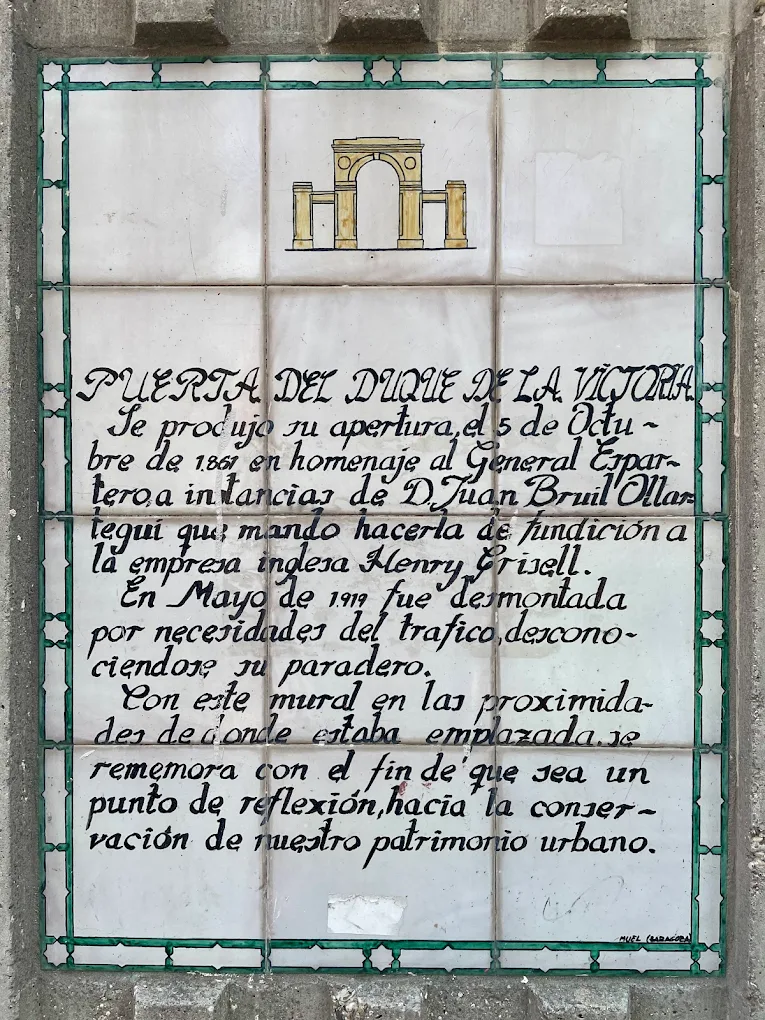 Placa cerámica conmemorativa junto al mural, con la historia resumida de la puerta